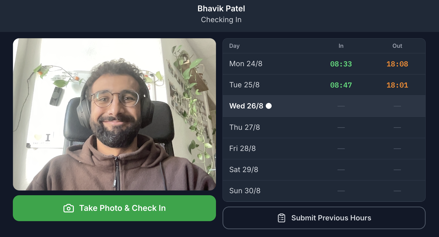 The Payrun check-in screen on a dark background. A name at the top with Checking In beneath it. On the left a live webcam view of someone at a desk, and a wide green button reading Take Photo & Check In. On the right a table of their week with Day, In and Out columns: Monday and Tuesday filled in with green clock-in and orange clock-out times, today marked with a dot, the rest of the week empty, and a Submit Previous Hours button underneath.